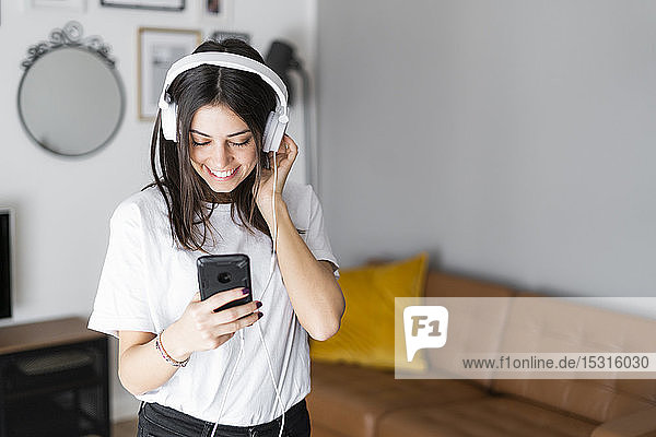 Happy young woman with smartphone and headphones at home