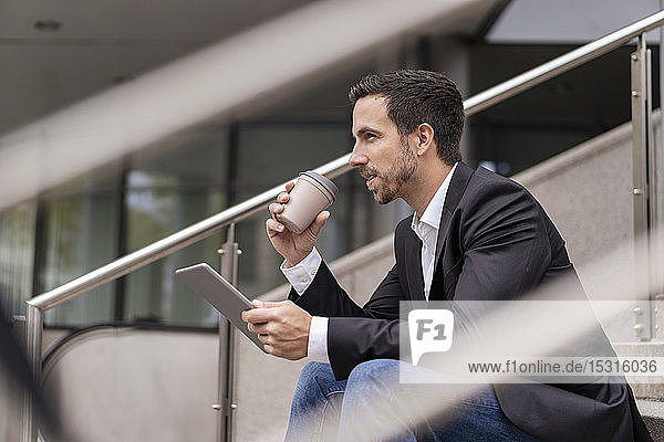 Geschäftsmann mit Tablette und Kaffee zum Mitnehmen  der auf einer Treppe in der Stadt sitzt