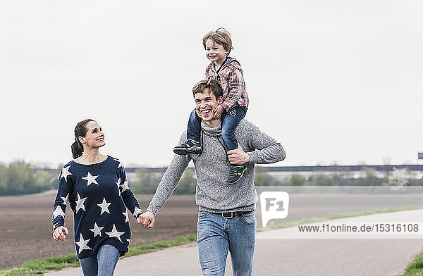 Glückliche Familie beim gemeinsamen Spaziergang neben den Feldern  Vater trägt Sohn huckepack