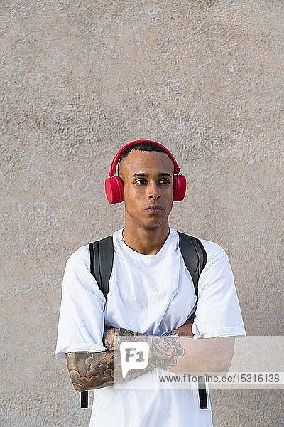 Porträt eines tätowierten jungen Mannes  der mit drahtlosen roten Kopfhörern Musik hört