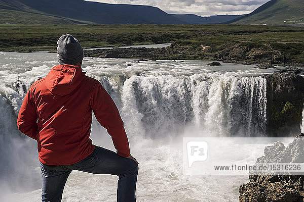 Mann betrachtet die Godafoss-Wasserfälle  Island  mit einem Fernglas