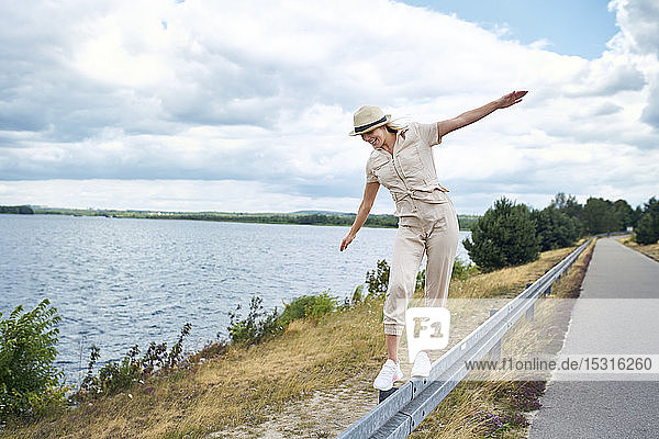 Glückliche Frau balanciert auf Leitplanke am Seeufer