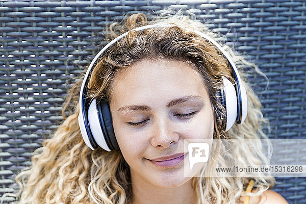 Lächelnde Frau  die mit geschlossenen Augen Musik hört und auf einem Liegestuhl liegt