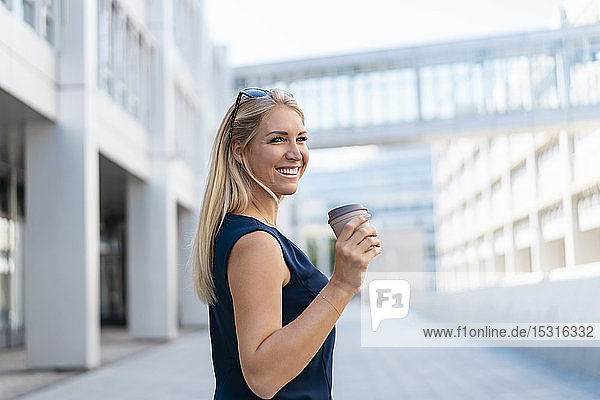 Porträt einer lächelnden blonden Geschäftsfrau mit Kaffee zum Mitnehmen im Sommer