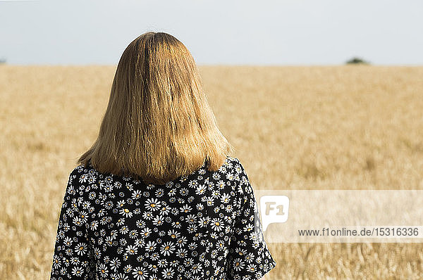 Rückenansicht einer Frau  die vor einem Getreidefeld steht