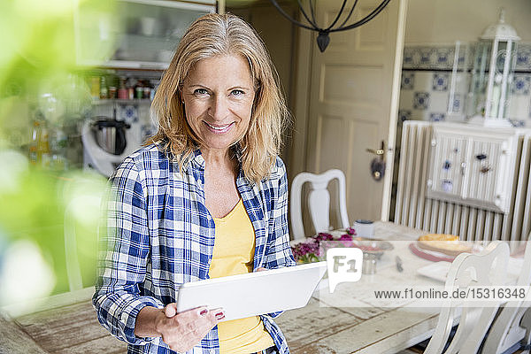 Porträt einer lächelnden reifen Frau mit digitalem Tablett in der Küche