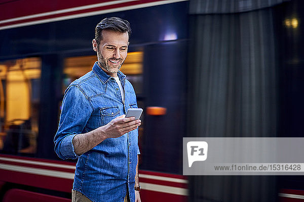 Mann benutzt Smartphone  während er in der Stadt mit der Straßenbahn im Hintergrund steht