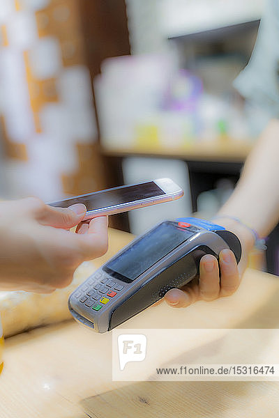 Kunden  die in einem Geschäft bargeldlos mit einem Smartphone bezahlen