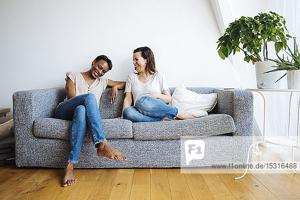 Zwei glückliche  entspannte Frauen sitzen zu Hause auf der Couch
