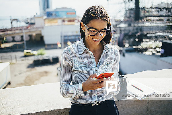 Lächelnde junge Geschäftsfrau überprüft Mobiltelefon im Freien