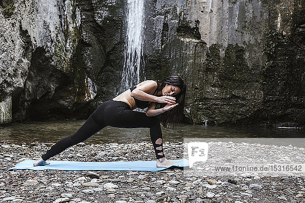 Frau praktiziert Yoga am Wasserfall  Dreieckshaltung