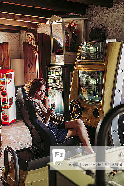 Young woman using cell phone in a driving simulator in a sports bar