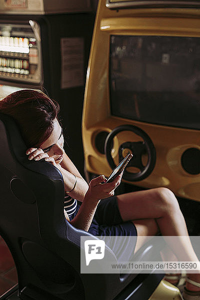 Junge Frau benutzt Handy in einem Fahrsimulator in einer Sportbar
