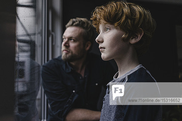 Boy and his father looking out of window on rainy day