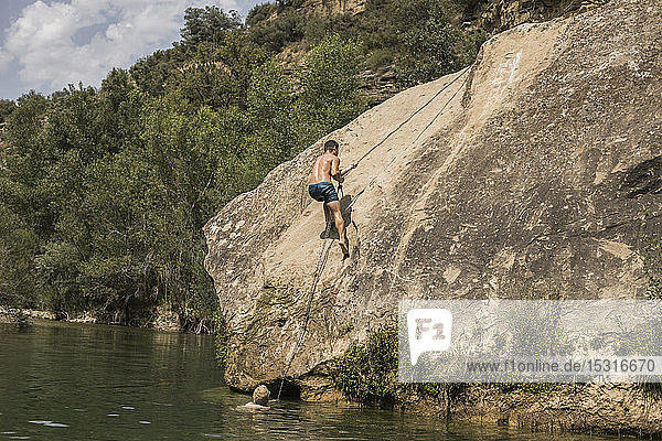 Junger Mann klettert auf einen Felsen an einem See  Spanien