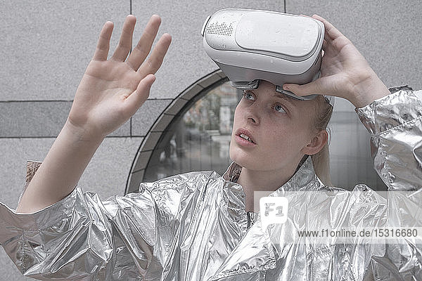 Mädchen im silbernen Anzug schaut durch eine VR-Brille und beobachtet ihre Hand