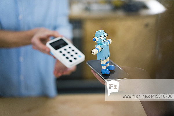 Customer paying contactless in a coffee shop  balancing toy robot on smartphone