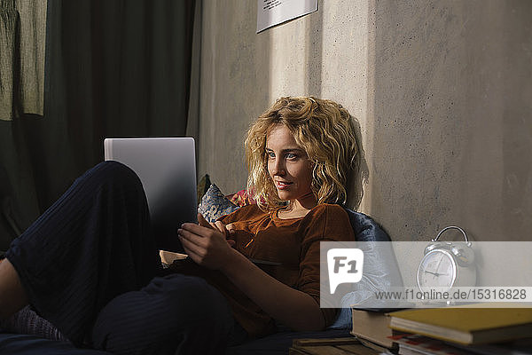 Porträt einer blonden jungen Frau  die mit einem Laptop auf dem Bett liegt