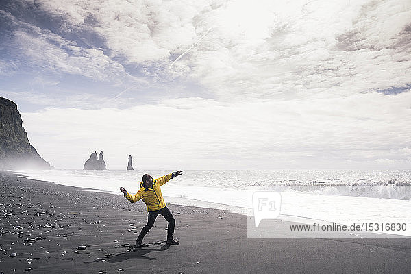Ein erwachsener Mann wirft einen Stein ins Meer  an einem Lavastrand in Island