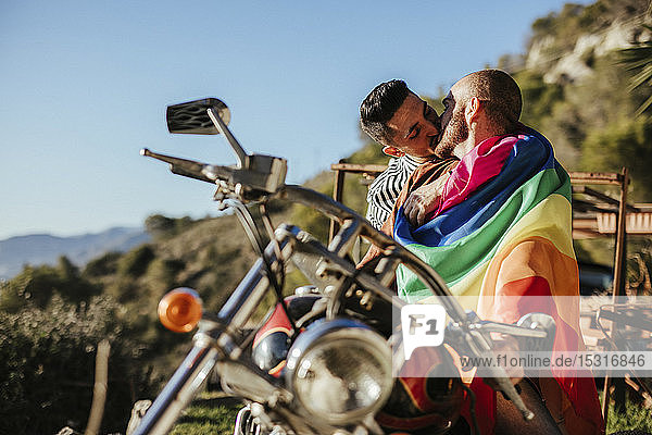 Schwules Paar mit schwuler Stolz-Fahne  das sich auf einem Motorrad küsst