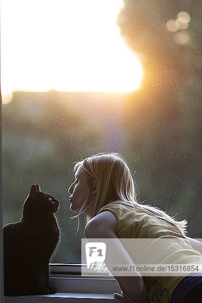 Schwarze Katze und Frau vor dem Fenster bei Sonnenuntergang