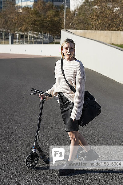 Junge Frau mit Sporttasche und Kickroller auf der Strasse