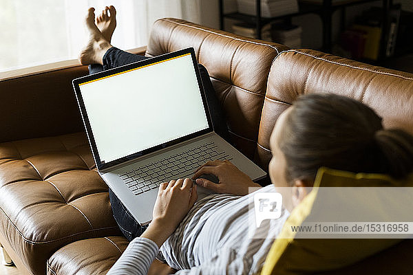 Young woman lying on couch at home using laptop