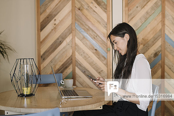 Junge Geschäftsfrau mit Laptop und Handy am Tisch in einem Café