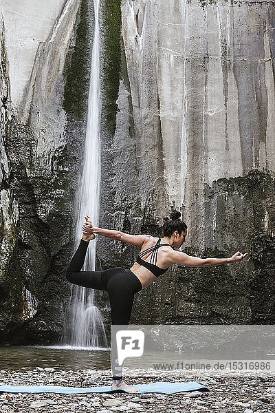 Frau praktiziert Yoga am Wasserfall