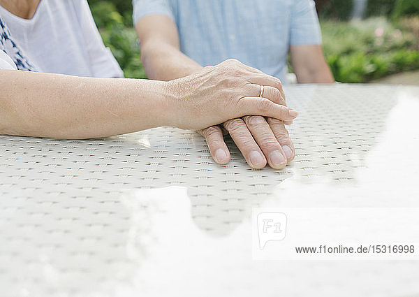 Älteres Ehepaar sitzt am Gartentisch und hält sich an den Händen  Nahaufnahme