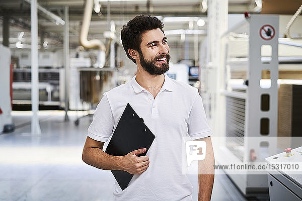 Smiling employee holding clipboard in a factory