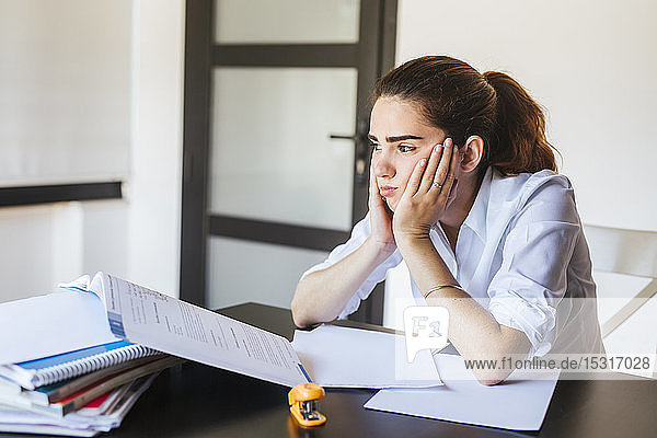 Frustrated female student with documents at desk at home