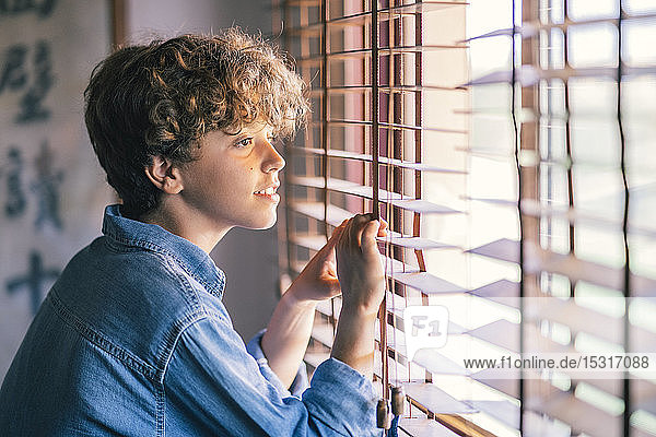 Junge am Fenster  der zu Hause durch Jalousien schaut