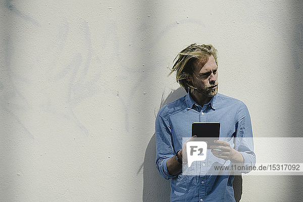 Young man with tablet at a wall looking around