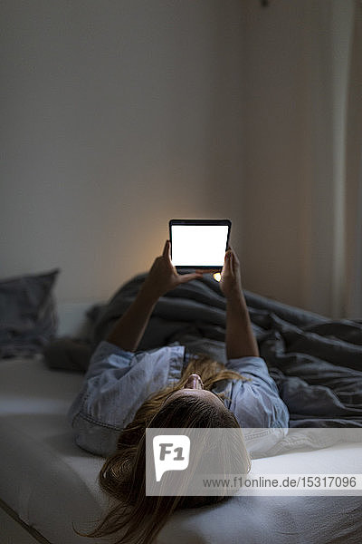 Young woman lying in bed at home at night using tablet