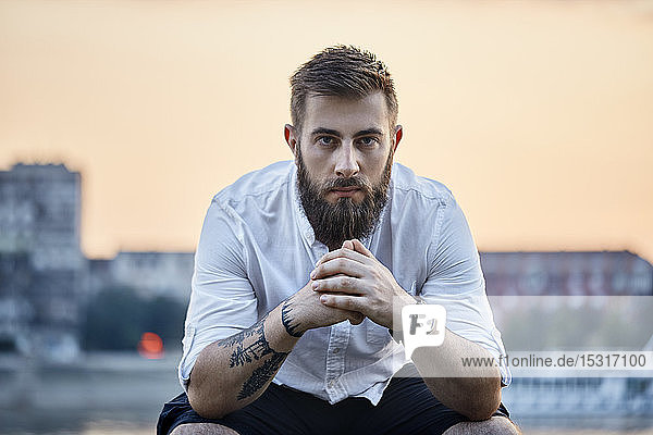 Portrait of a man with beard and tattoo sitting outdoors