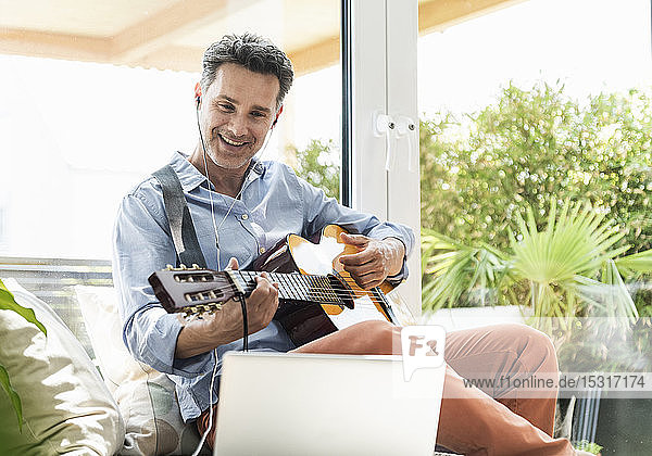 Mature man practising on the guitar using laptop and earphones