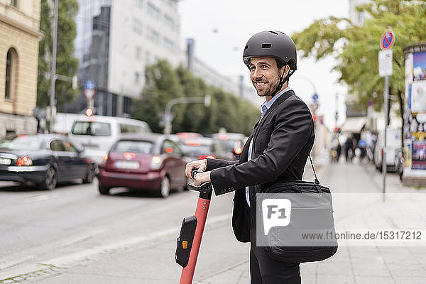 Smiling businessman with e-scooter in the city