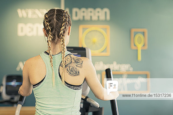 Rückansicht einer jungen Frau  die auf einer Steppmaschine im Fitness-Studio trainiert
