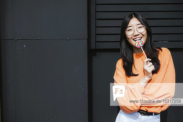 Young asian woman with lollipop in front of black wall