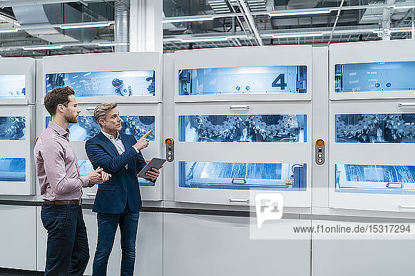 Two businessmen with tablet talking at machine in a modern factory