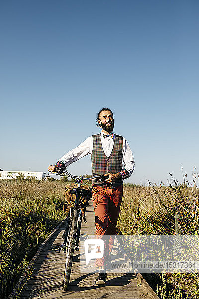 Well dressed man walking with his bike on a wooden walkway in the countryside after work