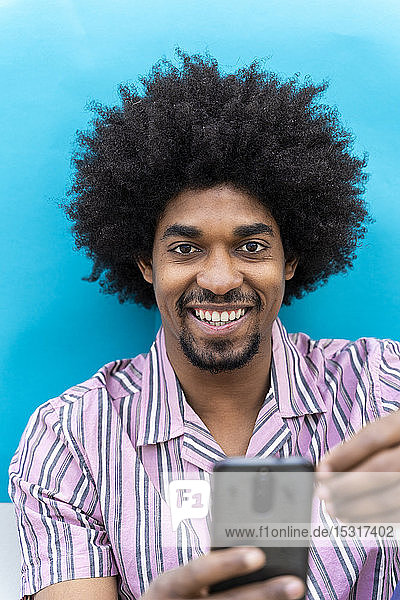 Lächelnder junger Mann mit Smartphone  blauer schwarzer Grund