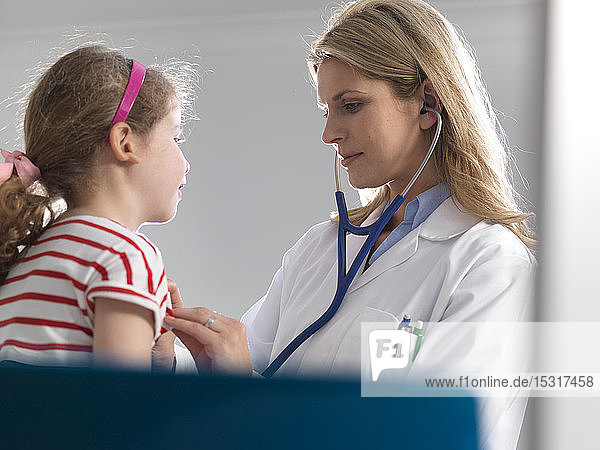 Ärztin  die in einer Klinik das Herz eines jungen Mädchens mit einem Stethoskop abhört