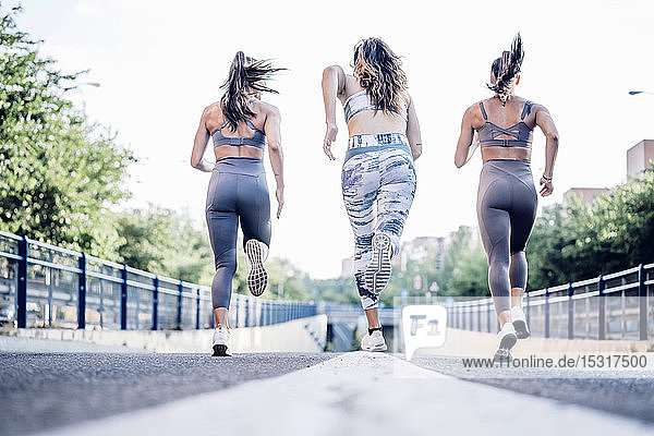 Three sporty young women running on a street