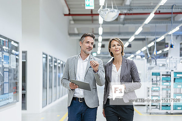 Geschäftsfrau und Geschäftsmann mit Tablette beim Gehen und Sprechen in einer modernen Fabrik