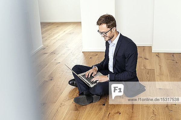Smiling businessman sitting on the floor using laptop