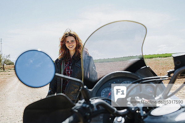Portrait of happy redheaded woman with motorbike on dirt track