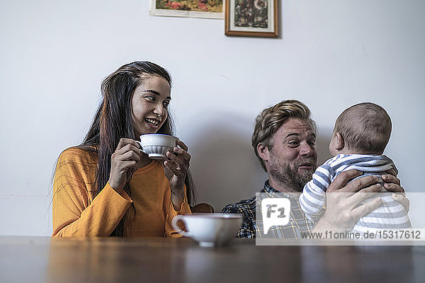 Happy family with baby sitting at wooden table at home