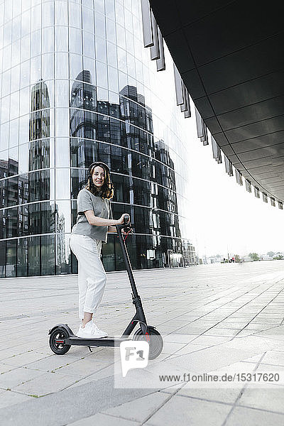 Frau mit E-Scooter und Helm  im Hintergrund moderne Bürogebäude